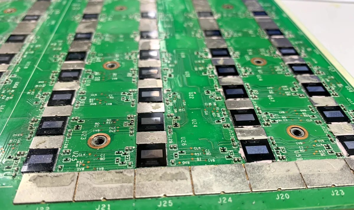 Placa hash de Antminer de cerca: filas de chips BM1398, serigrafía con las marcas CLK, RST, BI, BO, RO, las tensiones 0V8 y 1V8 y los conectores J20 a J25 en el borde
