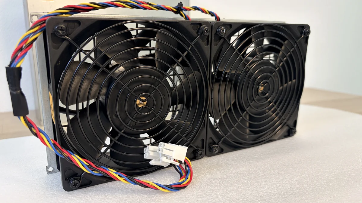 Par de ventiladores originales del minero sobre un soporte metálico común, con cables de cuatro hilos y conector blanco de alimentación