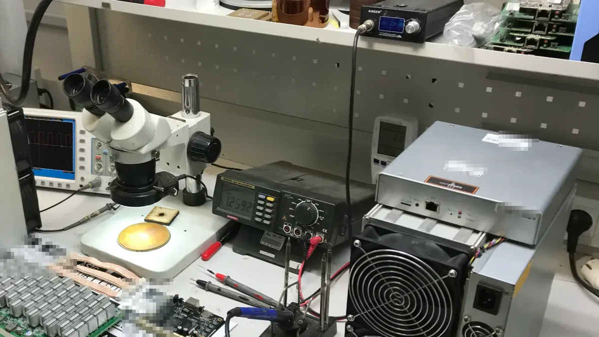 Taller de reparación de ASIC: microscopio estereoscópico, osciloscopio, multímetro de sobremesa midiendo y estación de soldadura, con una placa hash y una fuente al lado